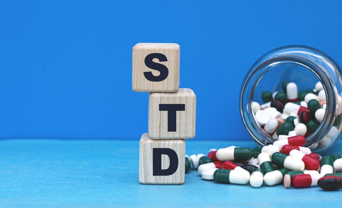 STD word on cubes on a blue background with a jar of tablets. Medical concept.