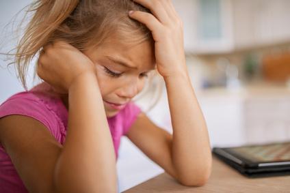 Beautiful little girl in pink dress sits at table and cries.