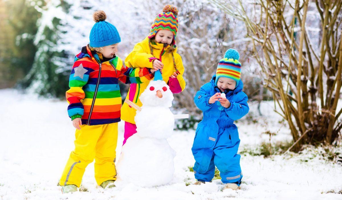 Children build snowman. Kids building snow man playing outdoors on sunny snowy winter day. Outdoor family fun on Christmas vacation. Boy and girl play snow balls. Winter clothing for baby and toddler.